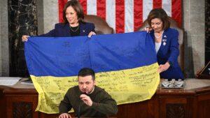 President Zelensky giving a speech while the Ukraine flag is held up