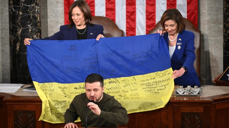 President Zelensky giving a speech while the Ukraine flag is held up