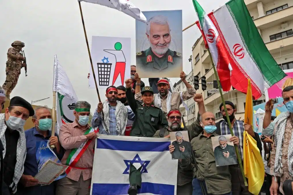 (Iranians prepare to set an Israeli flag on fire next to a picture of late Iranian general Qasem Soleimnai during a rally )
