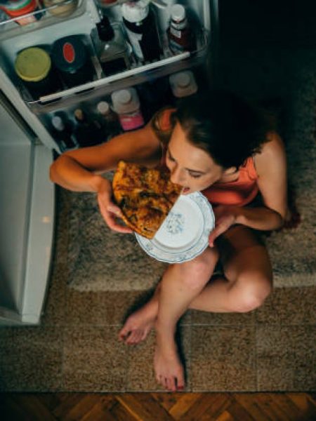 Woman eating in front of the refrigerator in the kitchen late night