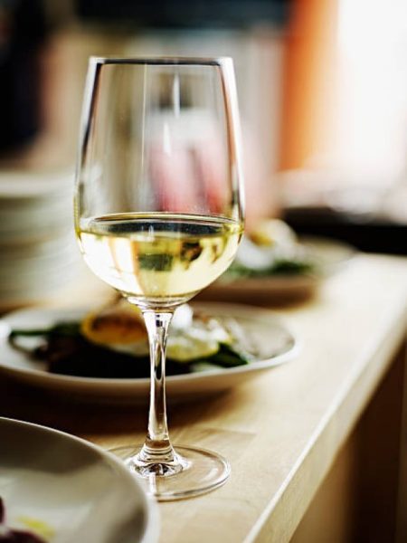 Glass of white wine sitting on countertop with plates of food