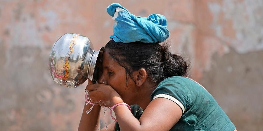 A woman drinks water as she waits for her turn to collect drinking water from a borewell of a temple complex in Ahmedabad.
