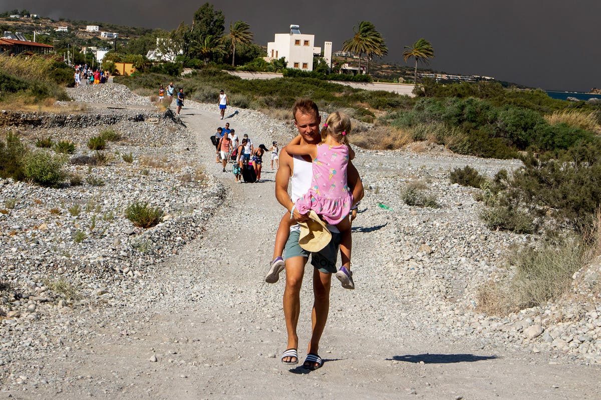 A man carries a child as they leave an area where a forest fire burns on the island of Rhodes