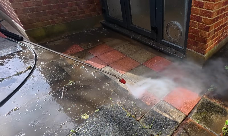 A man operates a pressure washer to clean a brick patio