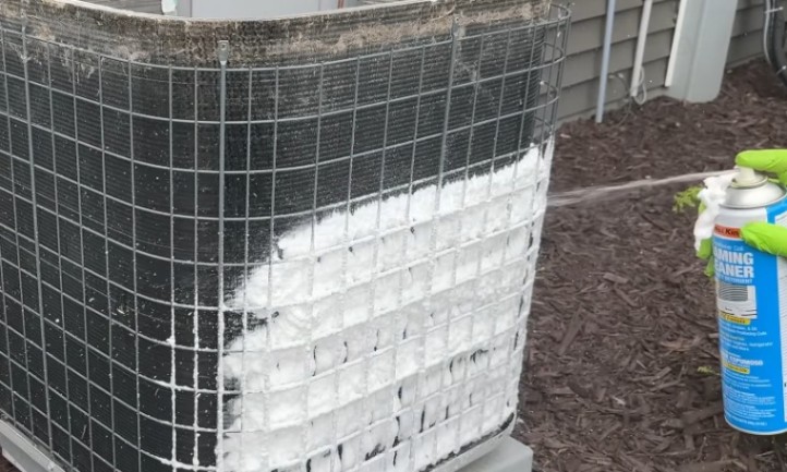 A man applying white foam to a heat pump, for maintenance or cleaning purposes