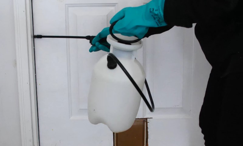 A person wearing black gloves is using a white spray bottle to apply a substance