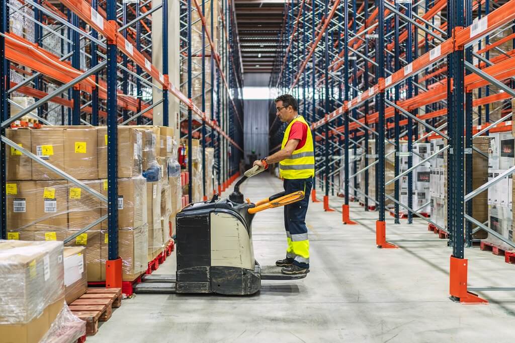 Warehouse worker handling pallet jack in organized logistics facility